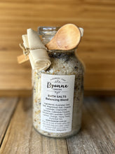 Jar of bath salts with a wooden spoon on a wooden surface, featuring Byanne Cosmetics branding.