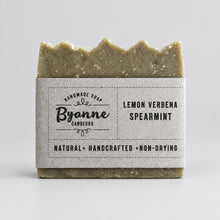 A handcrafted bar of soap Byanne Canberra, Lemon Verbena Spearmint, The soap is a muted sage green with a scalloped edge, wrapped in a kraft paper sleeve displaying the brand name and scent.